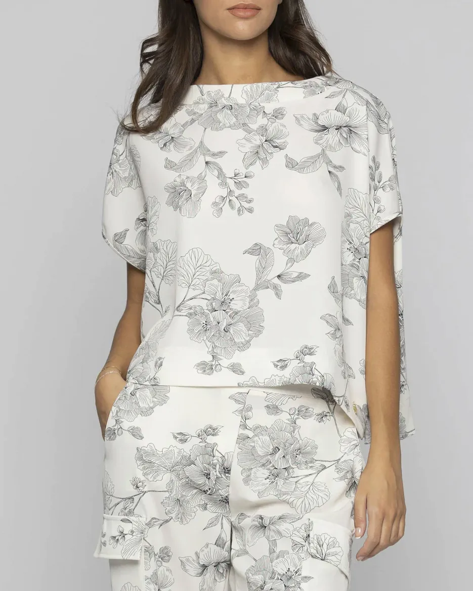 Blusa bianca cropped a fantasia fiori neri con scollo a barchetta e manica scesa