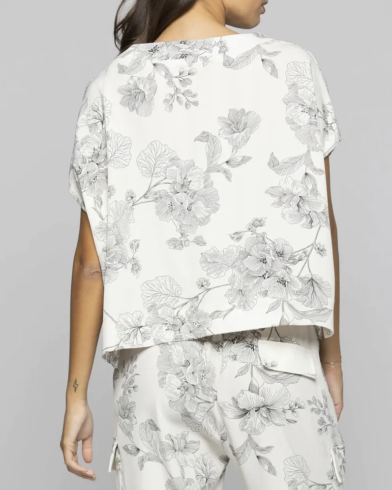Blusa bianca cropped a fantasia fiori neri con scollo a barchetta e manica scesa